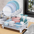 Two-tier stainless steel dish drying rack with utensil holder and drain board on a kitchen counter